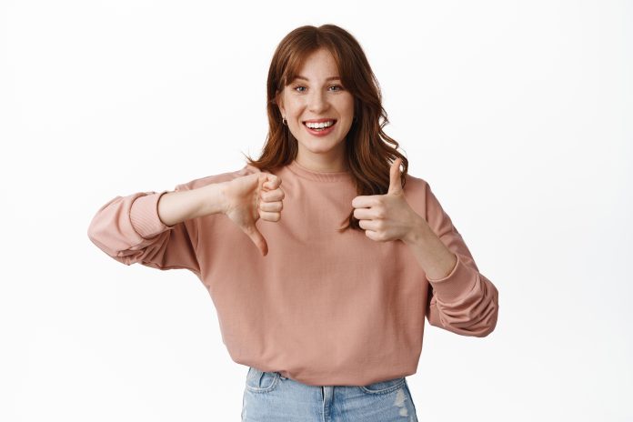 Smiling redhead female model, showing thumb down up, medium average rate, leave feedback, standing over white background Imagen de cookie_studio en Freepik