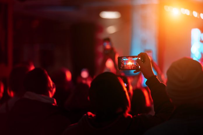 Person close up of recording video with smartphone during a concert.
