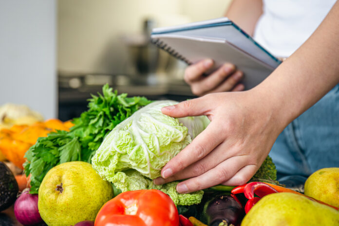 Woman with notepad and vegetables on the kitchen table preparing a recipe. Nueva pirámide nutricional de EE. UU. genera críticas por priorizar proteínas animales